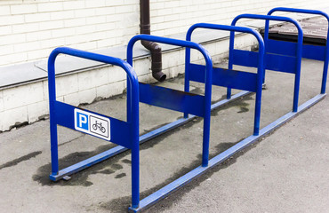 A metal bicycle park of blue color that stands in the city near the house. Abstract: safety, durable