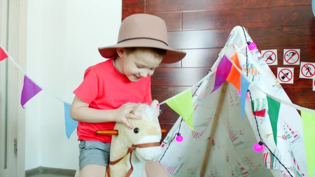 Little boy is riding a toy horse in the cowboy hat