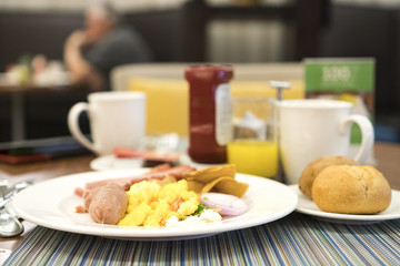 Breakfast on table served with egg, bread, thickness ham, orange juice, coffee in white ceramic cup, with blurry background.