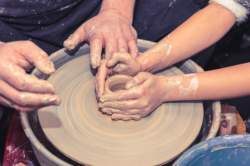 Little child learns how to sculpt a ceramic plate on a potter's wheel. Close-up of a child's hand.