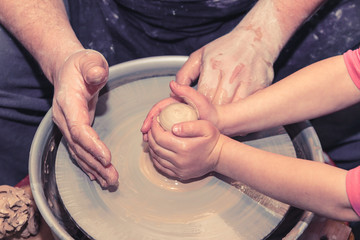 Little child learns how to sculpt a ceramic plate on a potter's wheel. Close-up of a child's hand.