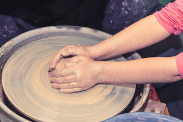 Little child learns how to sculpt a ceramic plate on a potter's wheel. Close-up of a child's hand.