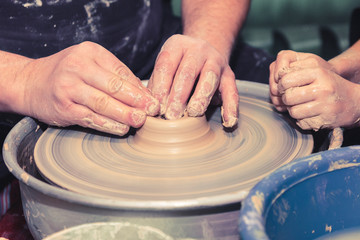 Men's and child's hands. Potter at work. Creating dishes. Potter's wheel. Dirty hands in the clay and the potter's wheel with the product. Creation. Working potter.