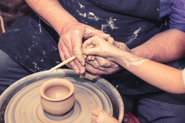 Senior potter teaching a little girl the art of pottery. Child working with clay, Creating ceramic pot on sculpting wheel. Concept of mentorship, generations. Arts lessons, pottery workshop for child