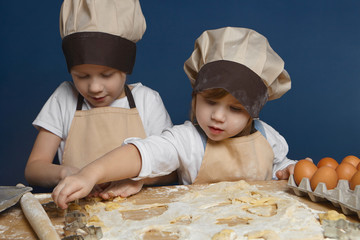 Two charming kids baking pastry together in kitchen, wearing chef uniforms, using metal cutters. Cute little girl making cookies with her elderly brother. Cooking, food, family and childhood