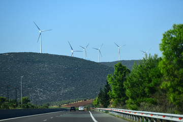 Windmills, wind generators on hill, mountain. Landscape with mountains, roads, trails, cars. Alternative energy sources concept. Giant white windmills on mountains.