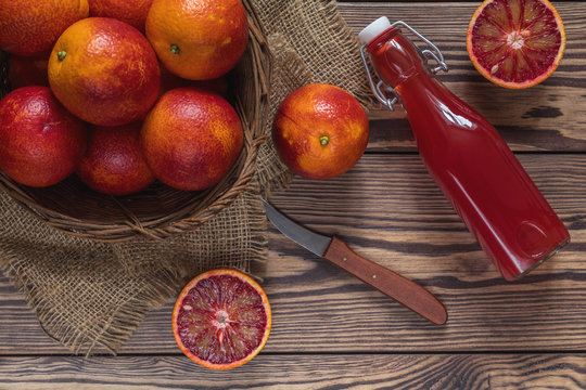 Blood orange fruit in a wicker basket and bottle juice on dark wooden table.