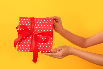 Young woman studio isolated on yellow in a red dress holding present box close-up