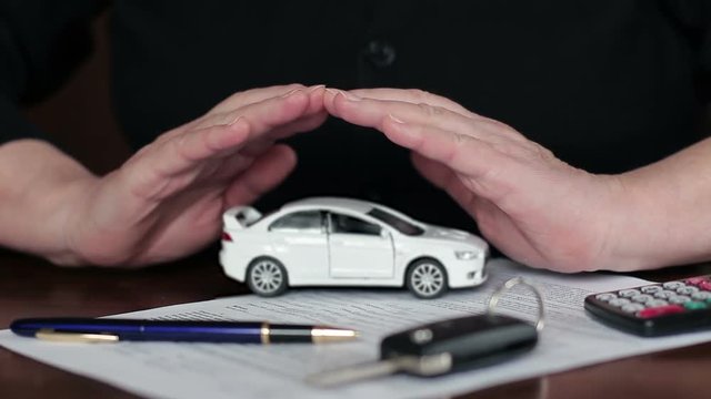 Female hands of an insurance agent protecting a small toy car. The concept of protection