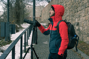 Professional travel and nature male photographer taking pictures on city with castle walls behind using a telephoto and tripod.