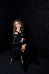 Fototapeta na wymiar Curly hair girl at leather jacket on studio against black brick wall.
