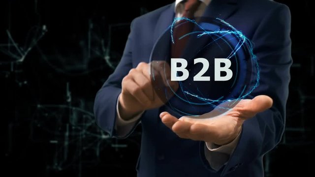 Businessman shows concept hologram B2B on his hand. Man in business suit with future technology screen and modern cosmic background