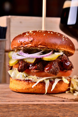 Fresh homemade hamburger with beef, onion, sause and cabbage garnish and dark beer on a wooden board, wooden table background. Juicey gourmet burger, fast food concept. Text place, copy space