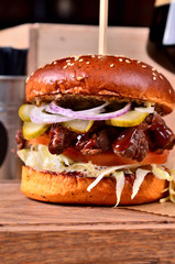 Fresh homemade hamburger with beef, onion, sause and cabbage garnish and dark beer on a wooden board, wooden table background. Juicey gourmet burger, fast food concept. Text place, copy space