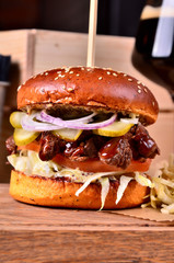 Fresh homemade hamburger with beef, onion, sause and cabbage garnish and dark beer on a wooden board, wooden table background. Juicey gourmet burger, fast food concept. Text place, copy space
