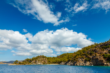 Fototapeta na wymiar Rocky coast with trees in the Aegean Sea. Big beautiful white clouds