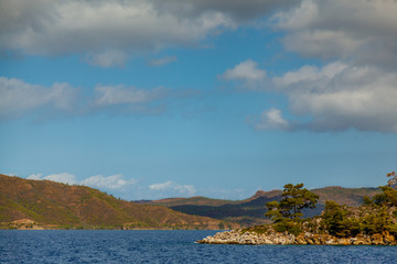 Obraz premium Rocky coast with trees in the Aegean Sea. Big beautiful white clouds