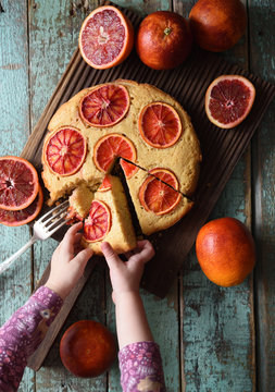 Dessert For Children. Baby Hands Reaching For Piece Of Blood Orange Cake On Oak Board On Shabby Blue Background