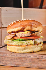 Top view Fresh homemade burger with chicken, salad, cheese, onion, cucumber, tomato, sause and dark beer on a wooden board, table background. Juicey gourmet roll bread, fast food concept. Text place