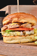 Top view Fresh homemade burger with chicken, salad, cheese, onion, cucumber, tomato, sause and dark beer on a wooden board, table background. Juicey gourmet roll bread, fast food concept. Text place