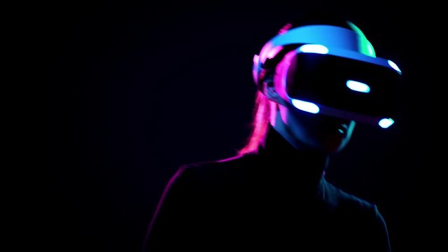 Young woman in VR headset have fun and play interactive game. Virtual reality helmet on black background