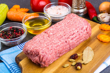 Fresh ground meat on wooden board with spices, vegetables