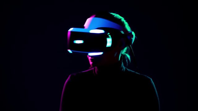 Young woman in VR headset looks around and wonders how amazing. Virtual reality helmet on black background