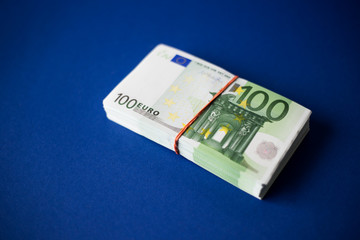 A stack of 100 euro bills tied with  rubber band on a dark blue background