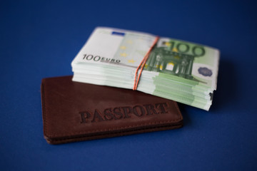 A stack of 100 euro bills tied with  rubber band on top of a passport on a dark blue background