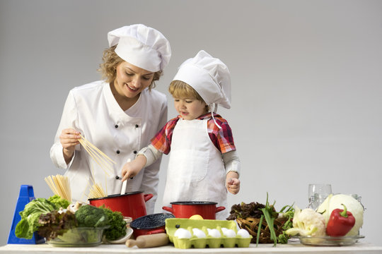 Mom and kid with smiling face cooking spaghetti together.