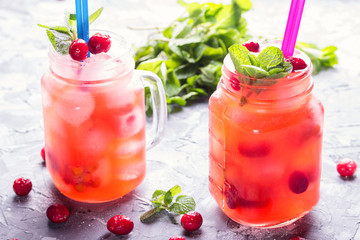 Berry cocktail of red currant and cowberry with ice and fresh mint leaves, with powdered sugar in cocktail drinking jars with colored drinking straws on a concrete table