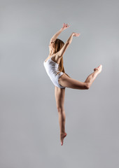 a young slender girl gymnast jumps high in the dance.