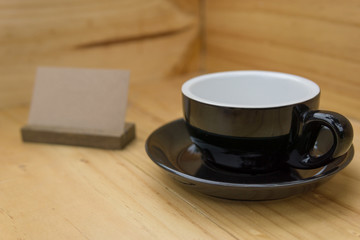 selective focus, close up of empty black coffee cup on the corner of wooden room or box with brown stand label. food or interior concept.