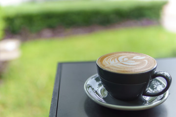 selective focus, close up of latte art coffee in black cup on the corner of table.