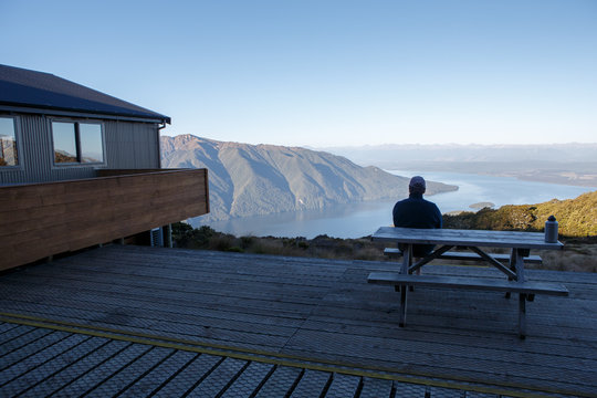 A hiker resting at the end of the day beside a hut on the Kepler Track.