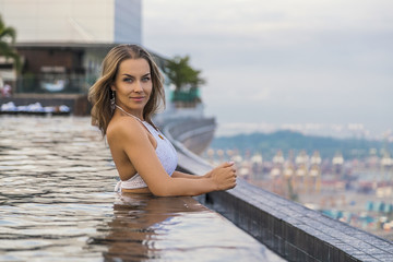 Fototapeta na wymiar молодая девушка в белом бикини в бассейне на крыше отеля марина бэй сандс 