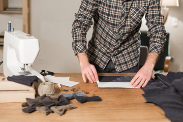 Cutting dark wool fabric. the line pattern. Young man working as a tailor and using a sewing machine in workshop.