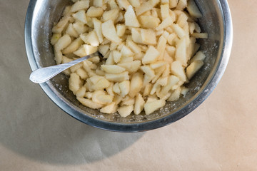 Chopped peeled pears mixed with sugar and a spoon in a metal bowl.
