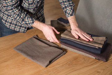 Selects wool from the stack. Young man working as a tailor and using a sewing machine in workshop.