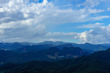 Obraz premium Amazing wild nature view of layer of mountain forest landscape with cloudy sky at winter season. Natural green scenery of cloud and mountain slopes background.