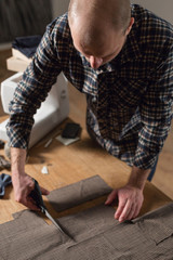 Closeup cutting brown plaid wool fabric. the line pattern. Young man working as a tailor and using a sewing machine in workshop.