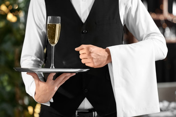 Waiter holding tray with glass of champagne in restaurant