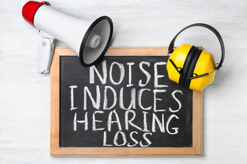 Headphones, megaphone and chalkboard with text NOISE INDUCES HEARING LOSS on table