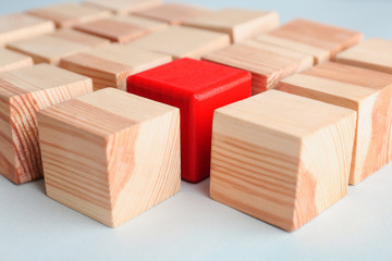 One red cube among wooden ones on table. Difference and uniqueness concept