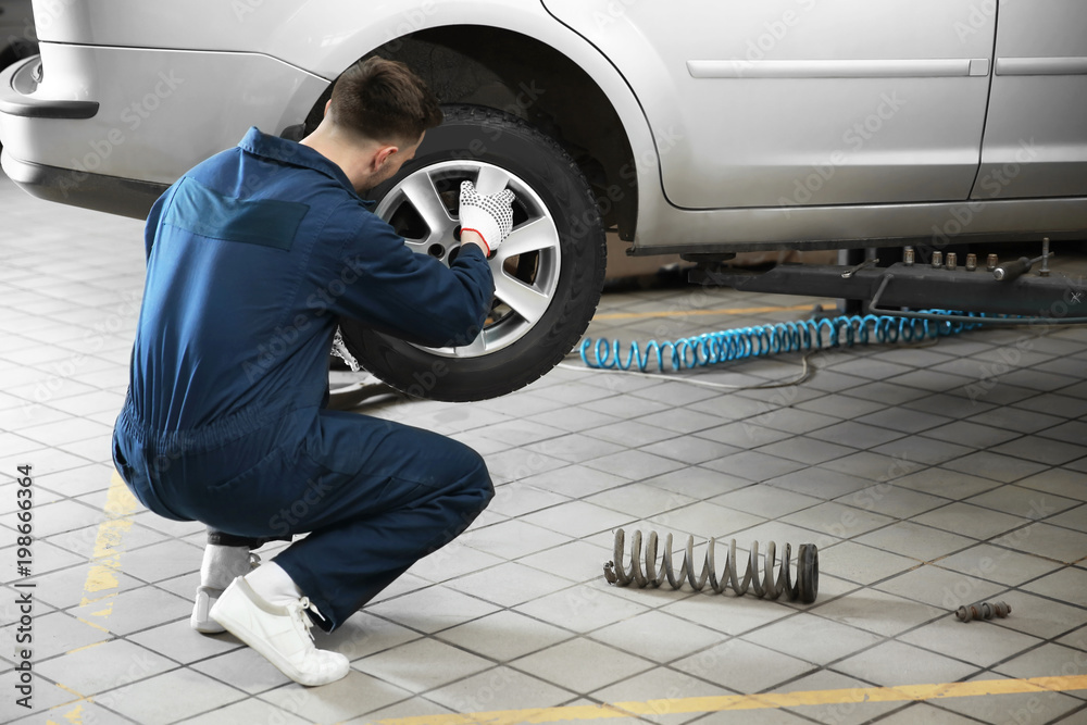 Poster Young mechanic changing wheel at tire service