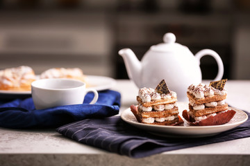 Plate with tasty pastries, teapot and cup on table