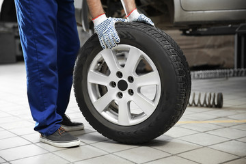 Fototapeta na wymiar Mechanic with car tire in service center, closeup