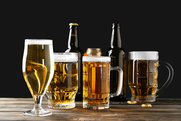 Different glassware with beer on wooden table against black background