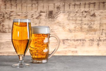 Glass and mug with fresh beer on wooden background