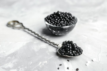 Spoon and bowl with delicious black caviar on grey background © Africa Studio
